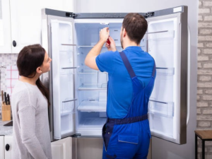 Woman Looking At Male Repairman Fixing Refrigerator With Screwdriver